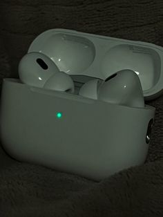 an apple airpods sitting on top of a white case with glowing green lights in it