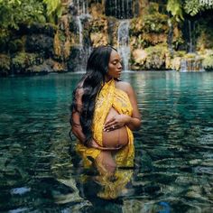 a pregnant woman standing in the water near a waterfall