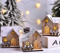 three small wooden houses sitting on top of a white box next to a christmas tree