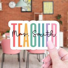 a person holding up a sticker that says teacher in multicolored letters on it