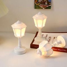 two white lamps sitting on top of a table next to a book