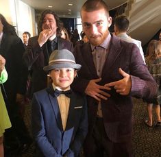 two men in suits and hats standing next to each other at a formal event with people looking on