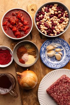 various foods are arranged in bowls on a wooden table, including beans and meats