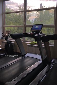 there is a laptop on the treadmill in front of a window with trees outside