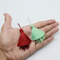 a person's hand holding two small tassels in their palm, one red and one green