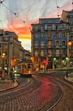 a cable car traveling down a street next to tall buildings at sunset with traffic lights in the foreground