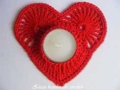 a crocheted heart shaped candle holder with a lit candle in the middle on a white surface