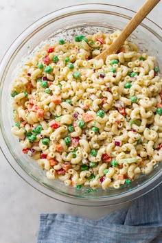 a bowl filled with macaroni and peas on top of a blue napkin next to a wooden spoon