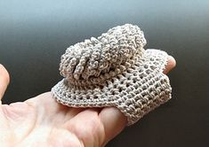 a hand is holding a crocheted hat on top of a black tablecloth