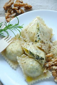 a white plate topped with ravioli covered in cheese and nuts next to a fork