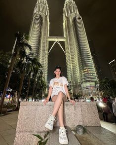 a woman sitting on a ledge in front of two tall buildings