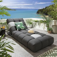 a large gray couch sitting on top of a patio next to a body of water