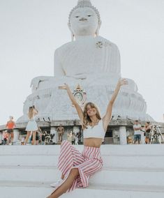 a woman sitting on steps in front of a large buddha statue with her arms up