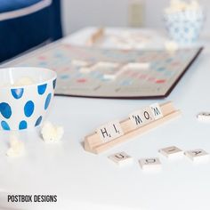 a wooden scrabble game with letters and dices on a table next to a bowl of popcorn