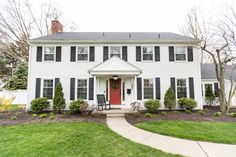 a white house with black shutters on the front and red door is shown in this photo