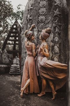 two women standing next to each other in front of a large rock structure with carvings on it