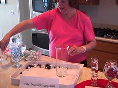 a woman in pink shirt pouring water into glasses on counter top with red plates and silverware