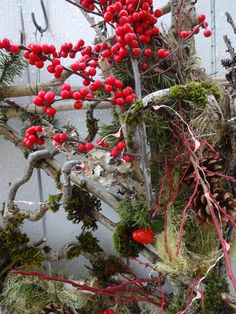 a bunch of branches with red berries and pine cones hanging from it's sides