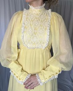 Details: maxi length; soft yellow; acetate lining with overlay; white lace trim toward bottom of skirt; around sleeve cuffs and at bodice; puffy, billowy, semi-sheer long sleeves with oversized button up cuff; lace bib detail; mock neck; attached front tie belt and zip up closure in the back.  Damage: minor separation under armpit seam on front lefthand sleeve; small stain on front layer toward hemline under lace trim; small spots on back hemline layer (well hidden in pleats); tears in acetate l Vintage Dresses With Sheer Sleeves For Spring, Cream Long Sleeve Billowy Dress, Yellow Long Sleeve Maxi Dress With Ruffles, Yellow Long Sleeve Ruffled Maxi Dress, Yellow Ruffled Long Sleeve Maxi Dress, Long Sleeve Lace Maxi Dress With Ruffles, Flowy Long Sleeve Maxi Dress With Lace Trim, Cream Long Sleeve Lace Maxi Dress, Cream Lace Long Sleeve Maxi Dress