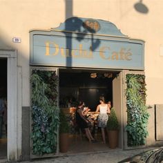 two women sitting at a table in the doorway of a cafe with potted plants