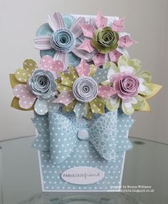 a card with paper flowers in a blue gift bag on a glass table, ready to be used as an ornament