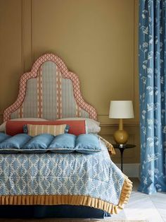 a bed with blue sheets and pillows in a bedroom next to a lamp on a table