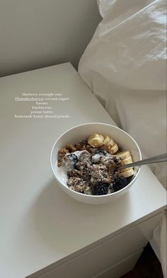 a bowl filled with cereal sitting on top of a white table next to a bed