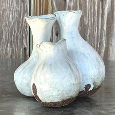 two white vases sitting on top of a table next to a wooden wall with peeling paint