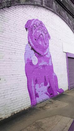 a purple pug painted on the side of a white brick wall next to a parking meter