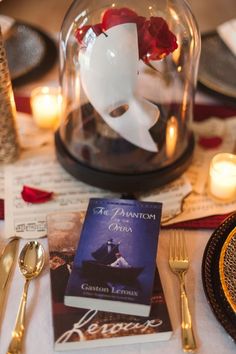 a table topped with books and candles next to a glass dome filled with flowers on top of a white cloth covered table