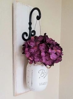 a white mason jar with purple flowers hanging from it's side on a wall