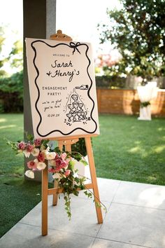 a sign that is sitting on top of a wooden easel with flowers in front of it