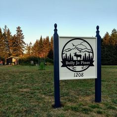 a sign in the middle of a grassy field with trees behind it and a building on the other side