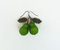 two green fruit shaped earrings with beads hanging from hooks on a white surface, one is made out of glass and the other is beaded with metal