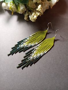 the green and white beaded earrings are next to some flowers on a gray surface