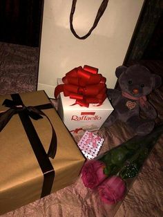 a teddy bear sitting next to a box with a red ribbon on it and two roses