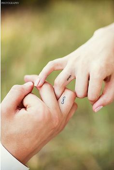 two people holding hands with tattoos on their fingers