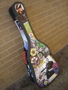 a guitar case that has been decorated with stickers on it and is leaning against a brick wall