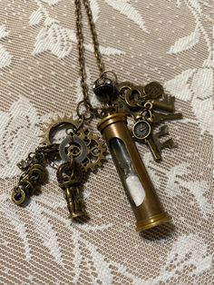 a necklace with an hourglass and keys attached to it on a lace tablecloth