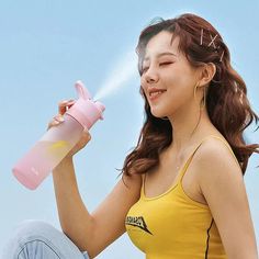 a woman sitting on the ground holding a pink water bottle and spraying it with her hand