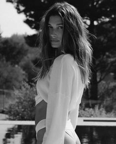 a black and white photo of a woman with long hair posing in front of a pool