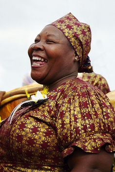 a woman in a dress smiles as she stands next to other women wearing headgear