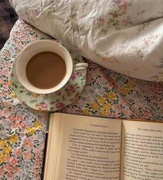 a cup of coffee and an open book on a bed with floral bedspread