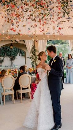 a bride and groom sharing a first dance under a canopy with flowers hanging from the ceiling