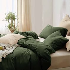 an unmade bed with green sheets and pillows on it in front of a window