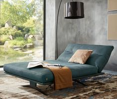 a blue chaise lounge chair sitting on top of a rug next to a window