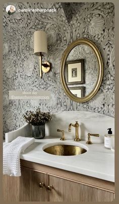 a bathroom sink under a mirror next to a gold faucet and wall paper