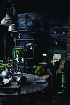 an old fashioned table and chairs in a room with dark walls, wooden floors and plants on the shelves