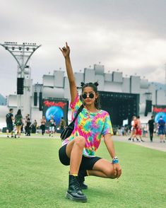 a woman kneeling on the ground with her arms in the air while wearing sunglasses and a tie dye t - shirt