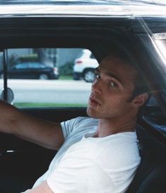 a man sitting in the passenger seat of a car with his hand on the steering wheel